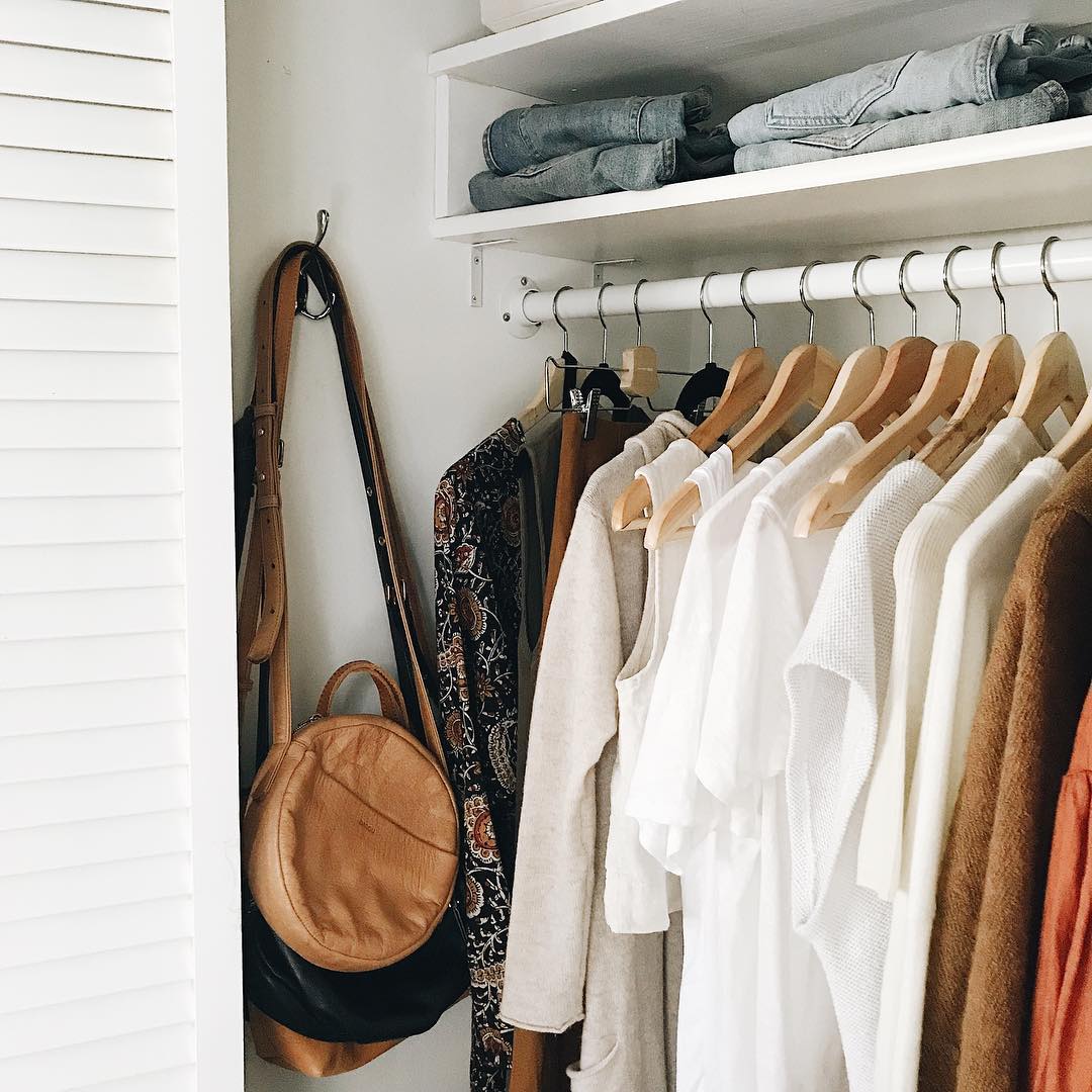 Closet filled with neutral-colored clothes and brown purse. Photo by Instagram user @caroline_joy