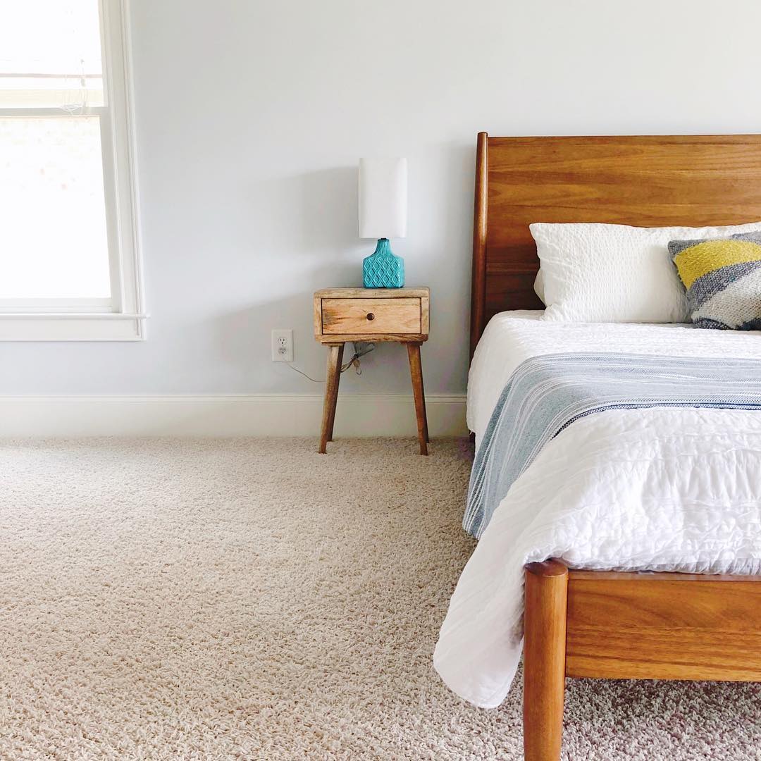 Bed with dark wood frame by light brown nightstand with blue lamp. Photo by Instagram user @raisingsimple