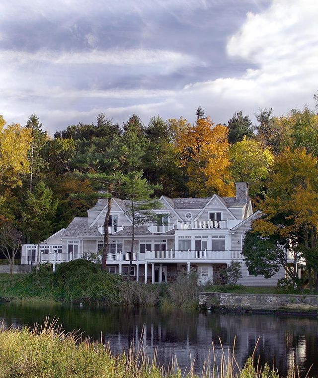Exterior photo of a large, mansion-like white clapboard house in fall. Photo by Instagram user @smirosarchitects