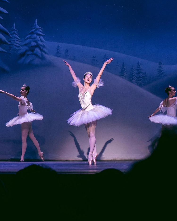 Ballerina standing on pointe with her arms raised and two others behind her. Photo by instagram user @alyssamariemuna