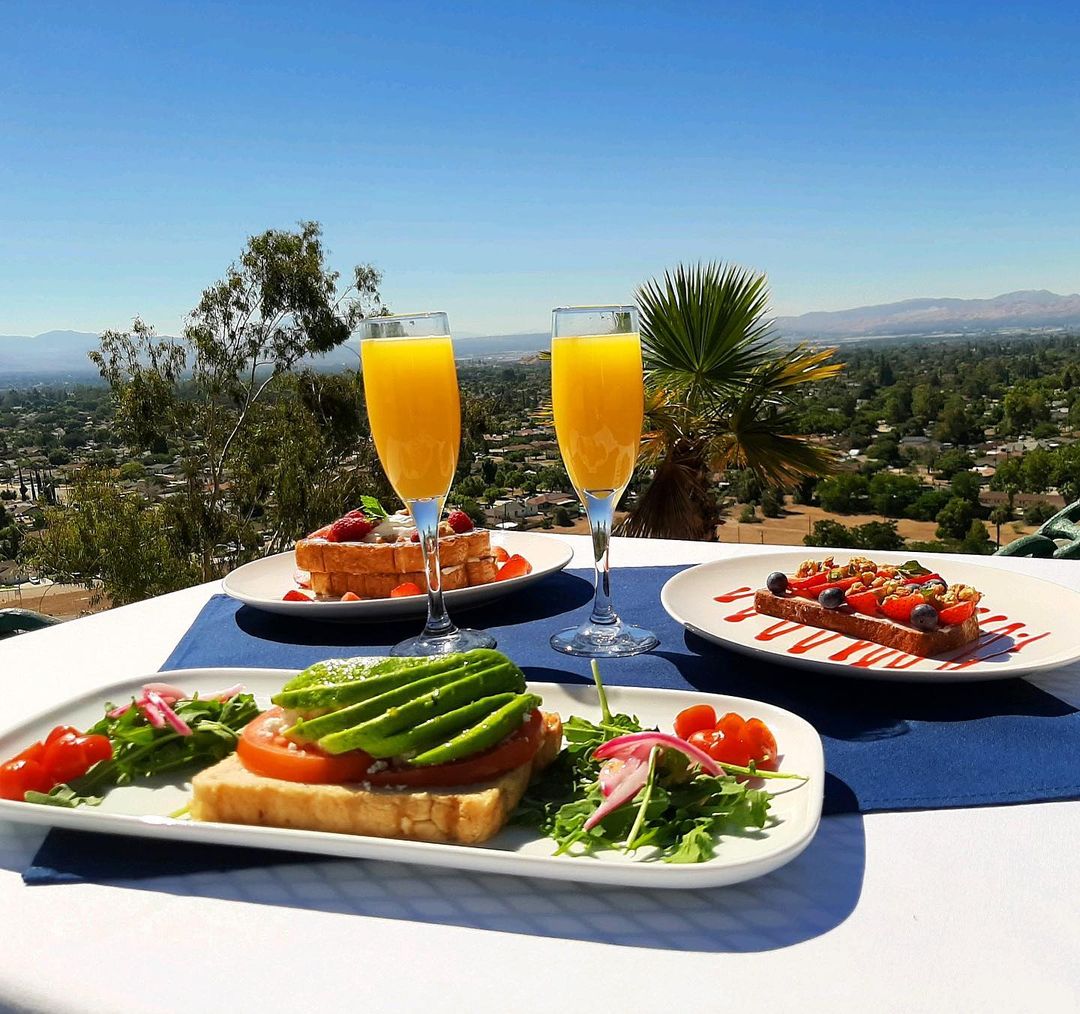 Three plates of brunch food and two mimosas on a table overlooking a landscape of trees and blue sky. Photo by Instagram user @hilltopcollection