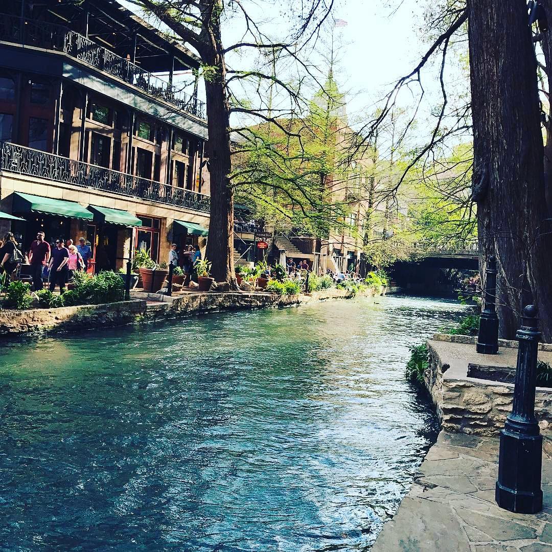 View of San Antonio River Walk with people walking on the opposite side. Photo by Instagram user @visitsanantonio