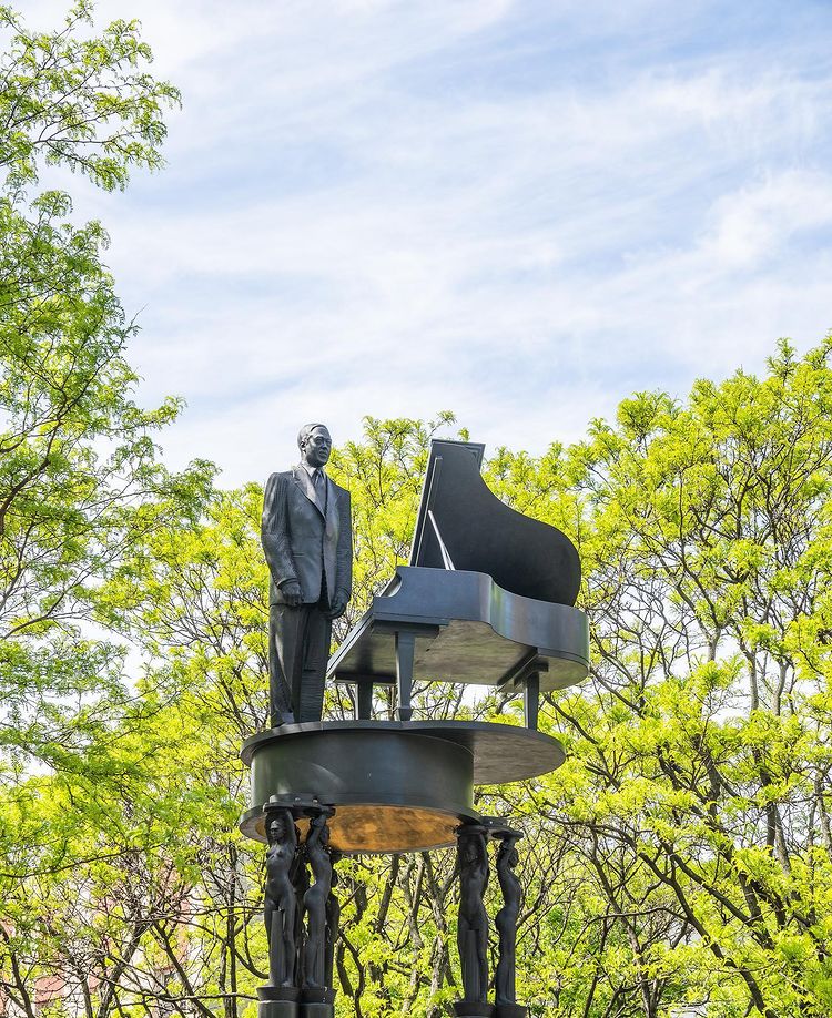 Duke Ellington statue surrounded by green trees. Photo by Instagram user @quintetnyc