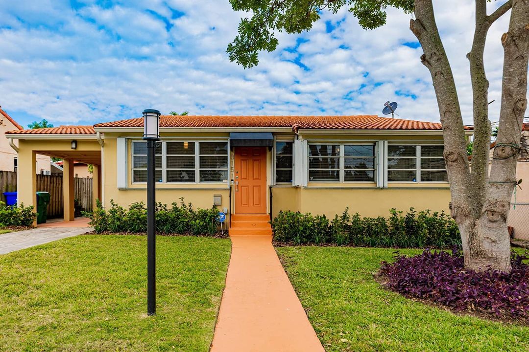 Yellow single-story home with a green lawn and orange sidewalk leading to front door in the Little Havana neighborhood in Miami