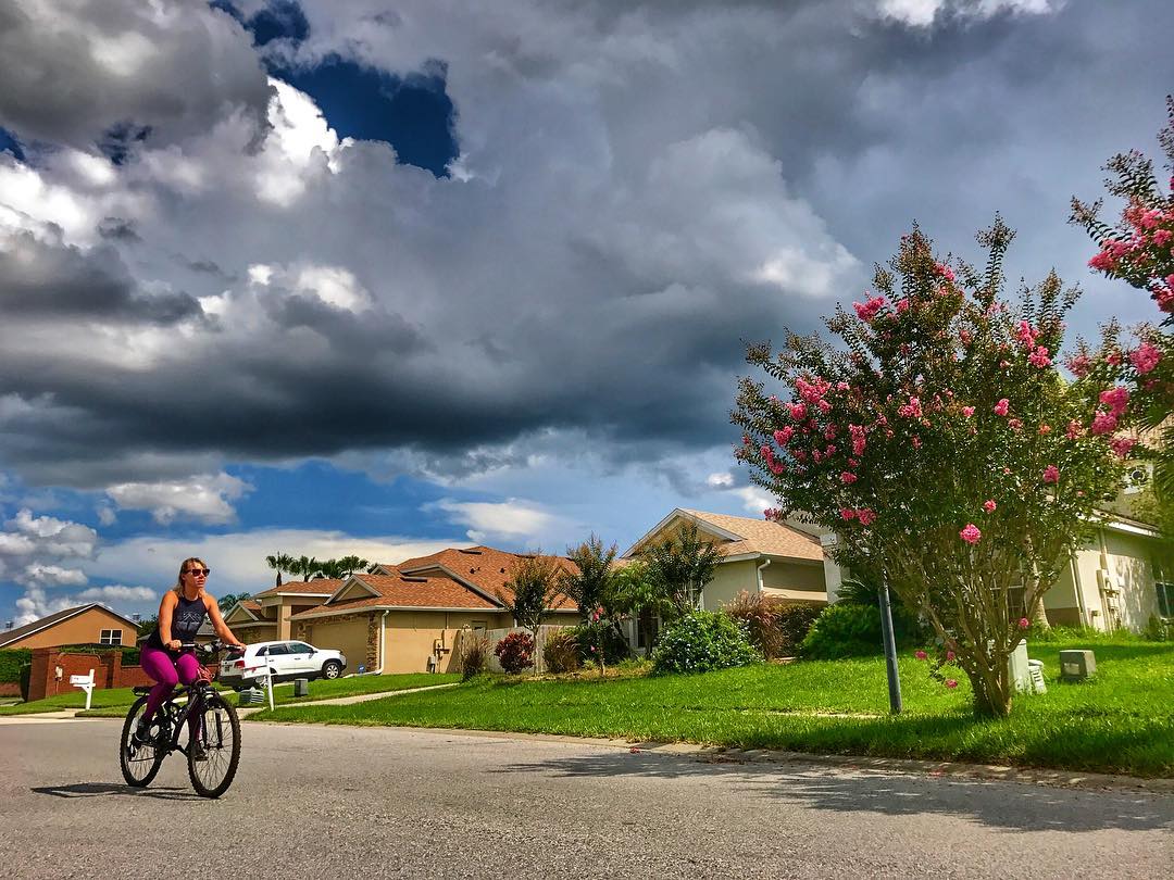 Dark clouds above a street of homes as a woman rides her bike. Photo by instagram user @kate.francis.fitness