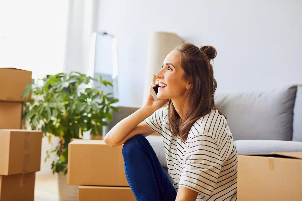 Young woman talking on phone with moving boxes around her