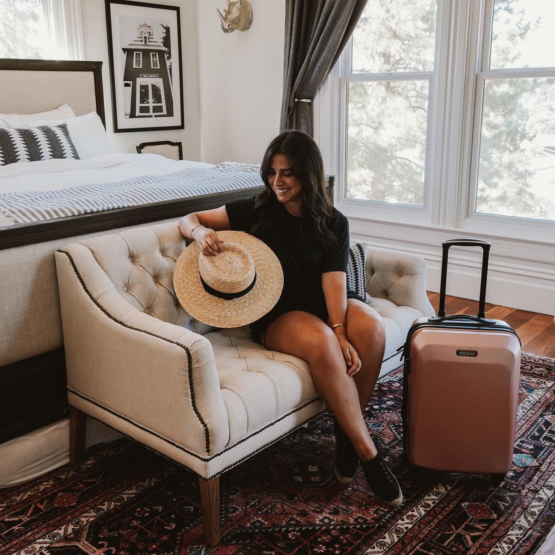 Young woman sitting in bedroom with suitcase. Photo by Instagram user @amtourister