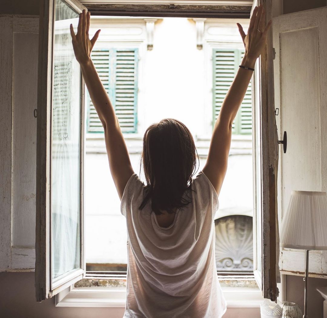 Woman stretching in front of window. Photo by Instagram user @vohanwellness