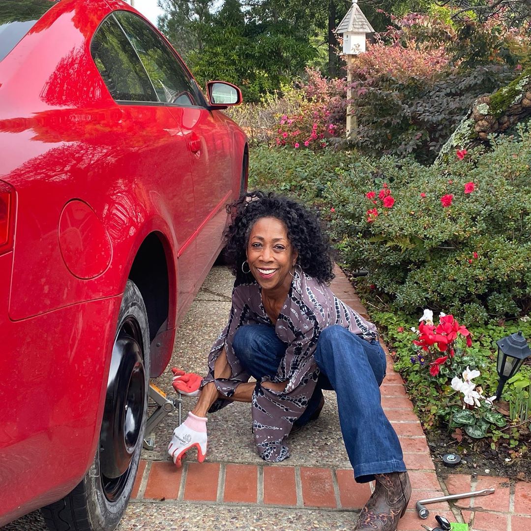 Woman changing tire on red car. Photo by Instagram user @bous_yoga