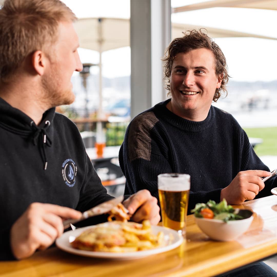 Two men sitting by each other sitting food. Photo by Instagram user @derwentsailingsquadron