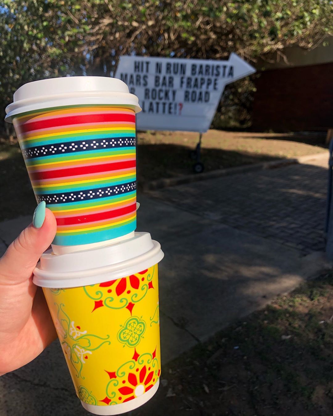 Hand holding two colorful cups of coffee. Photo by Instagram user @hitnrunbarista