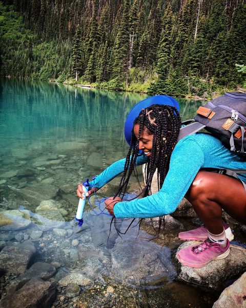 A female hiker kneeling down next to a river to use the LifeStraw product.