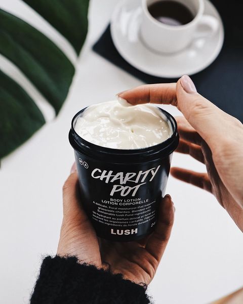 A hand holding a lush charity pot of lotion with a finger dipping into the lotion.