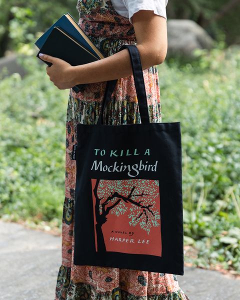 a person wearing an out f print tote bag while carying several books and walking.