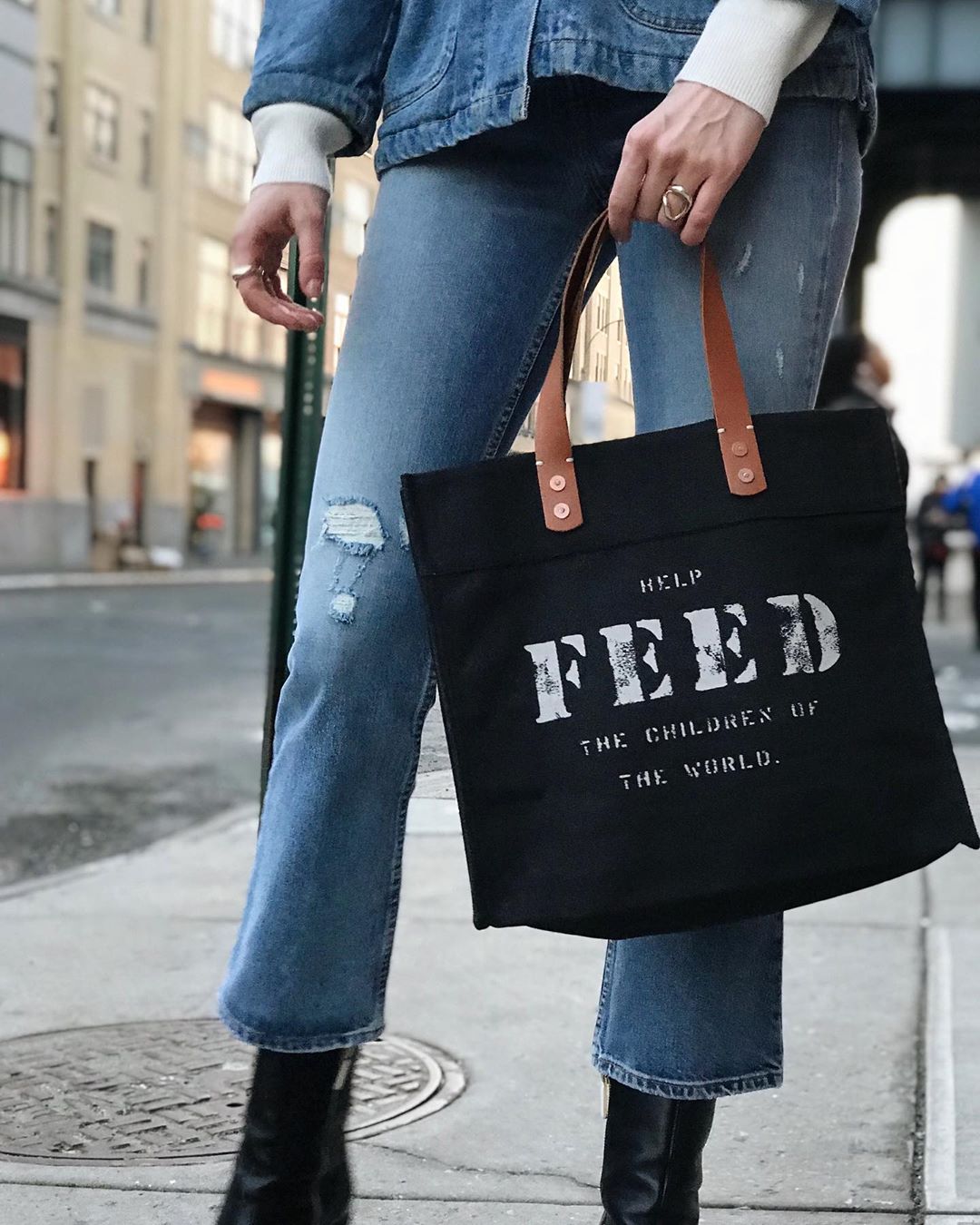 woman holding black FEED tote bag with brown leather handle. Photo by Instagram user @feed