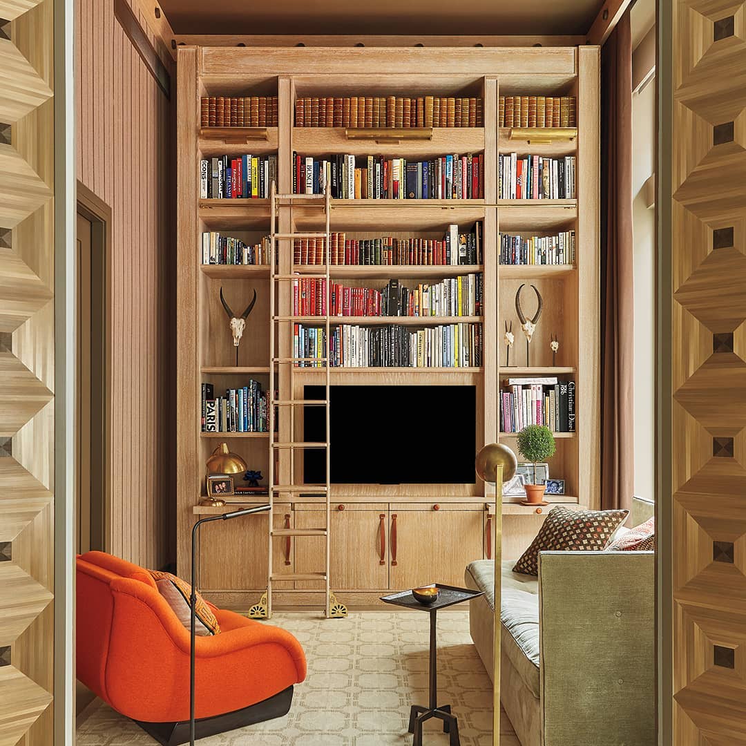 modern home library with large ladder and tv in middle photo by Instagram user @cottagesgardens