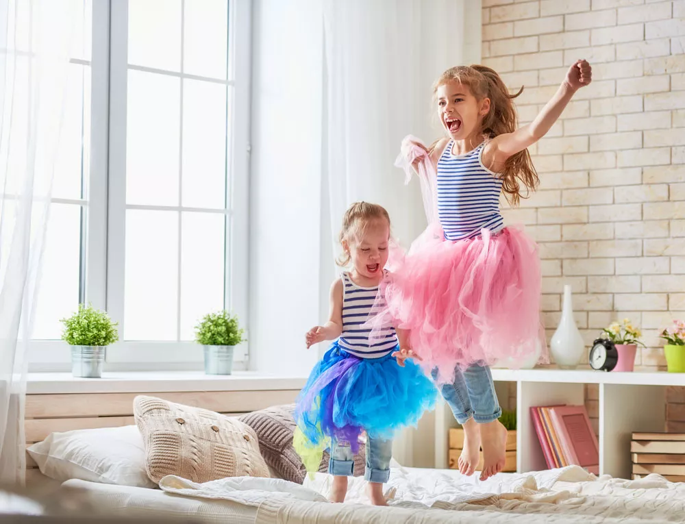 Little girls in shared bedroom jumping on bed