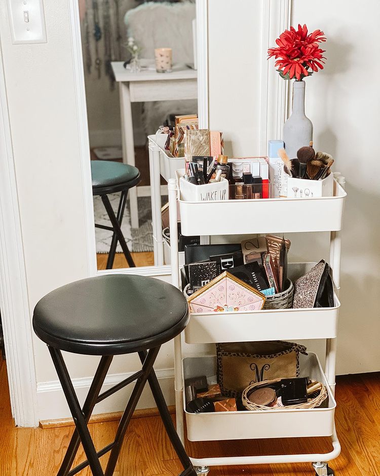 White rolling cart with makeup items in front of a mirror next to a black stool. Photo by Instagram user @caitlinoliviastyled
