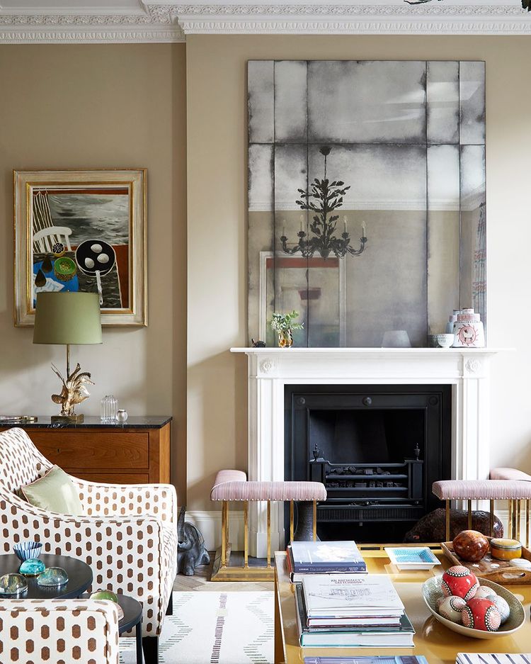 Light living room with books stacked on coffee table, an accent chair, and fireplace. Photo by Instagram user @annastathakiphoto.