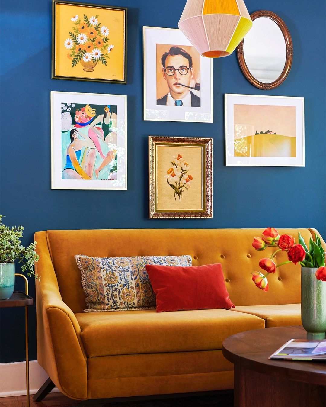 Colorful gallery wall on a blue accent wall above an orange couch. Photo by Instagram user @joybird.