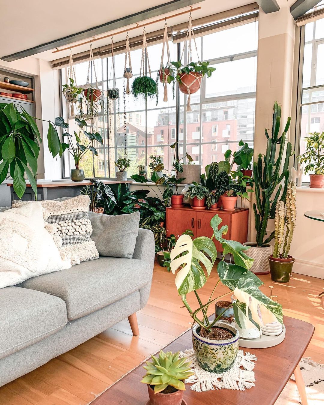 Living room with plants hanging from the ceiling, on the floor, and on shelves. Photo by Instagram user @themacramejungle.