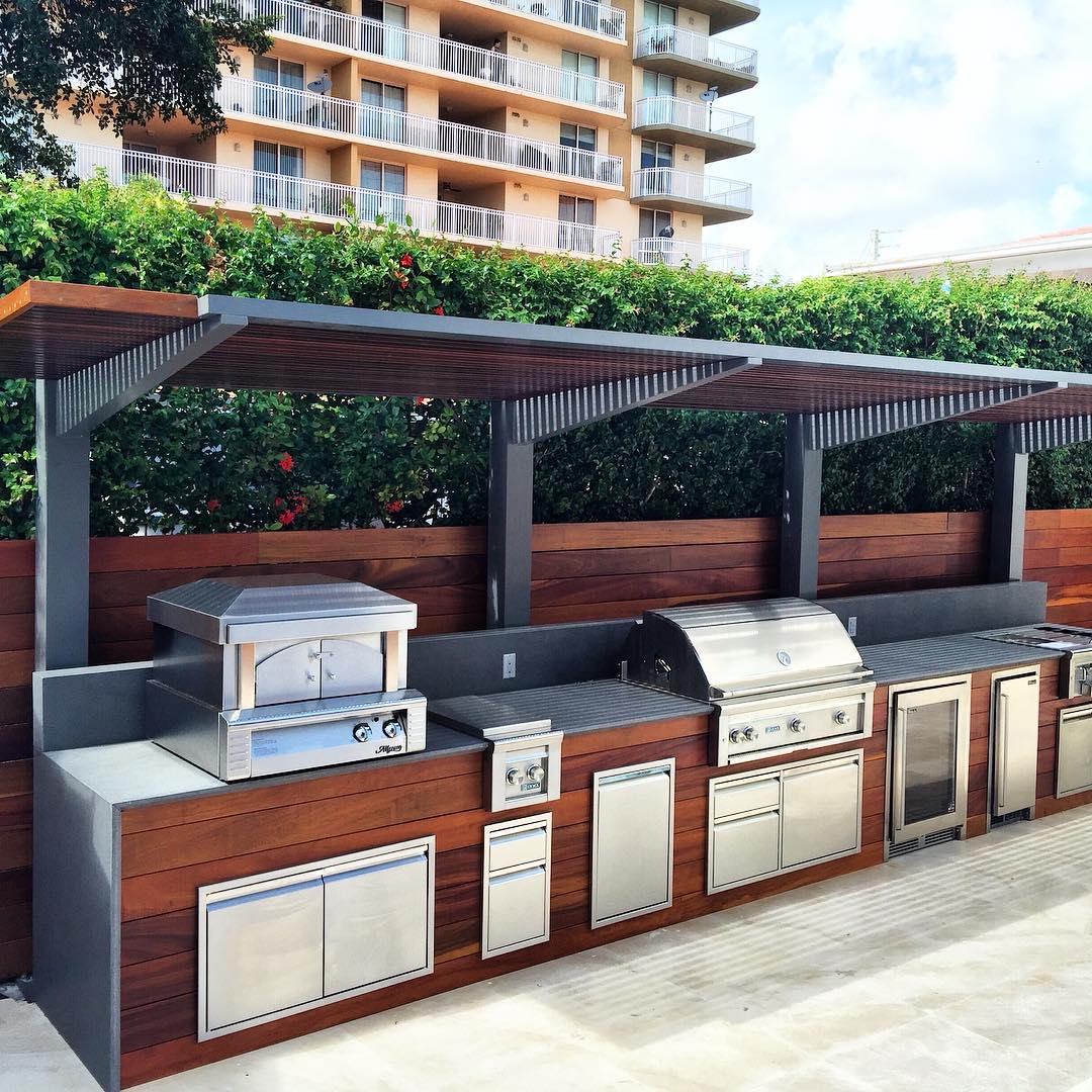 modular outdoor kitchen area built with grill, stove burners, pizza over, and fridge photo by Instagram user @luxapatio