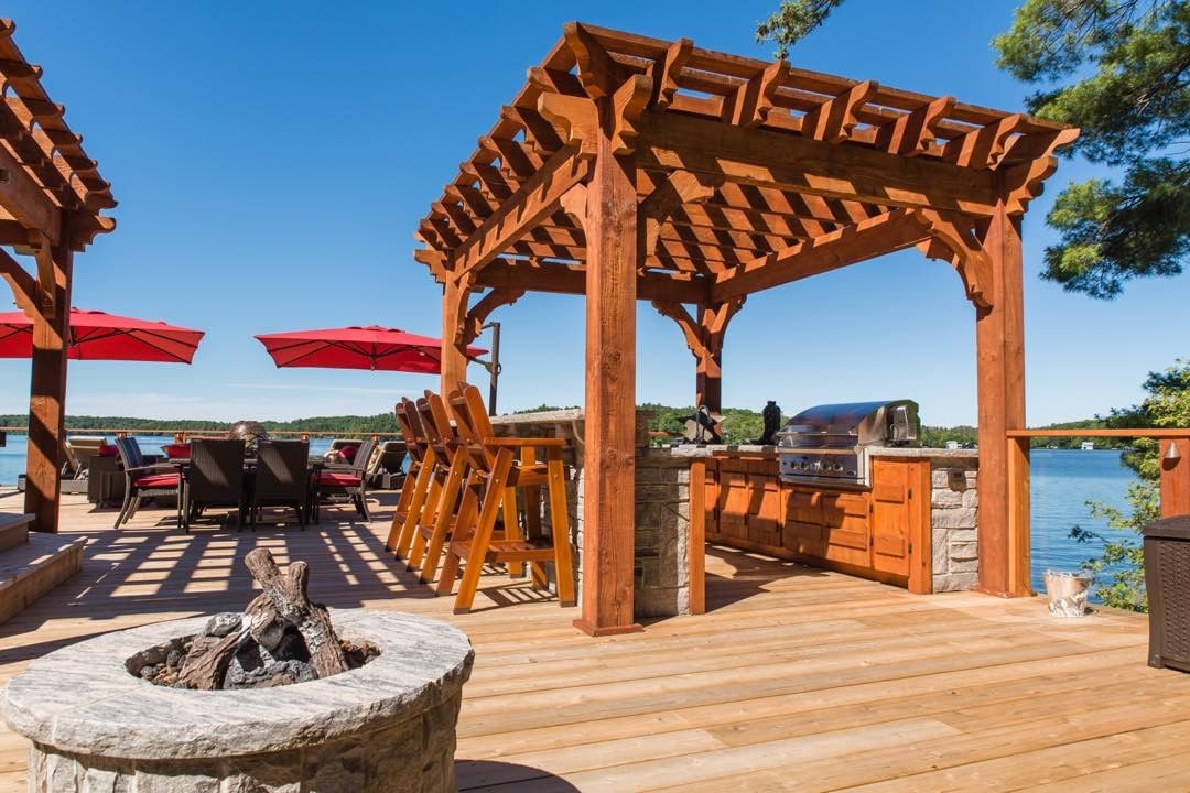 outdoor kitchen built into an open deck concept with full pergola photo by Instagram user @muskokalandscapers.ca