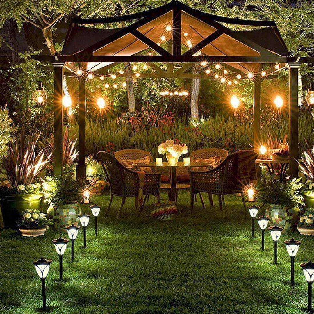 small dining set under a pergola with garden lighting leading to seats in grass photo by Instagram user @have2havehome