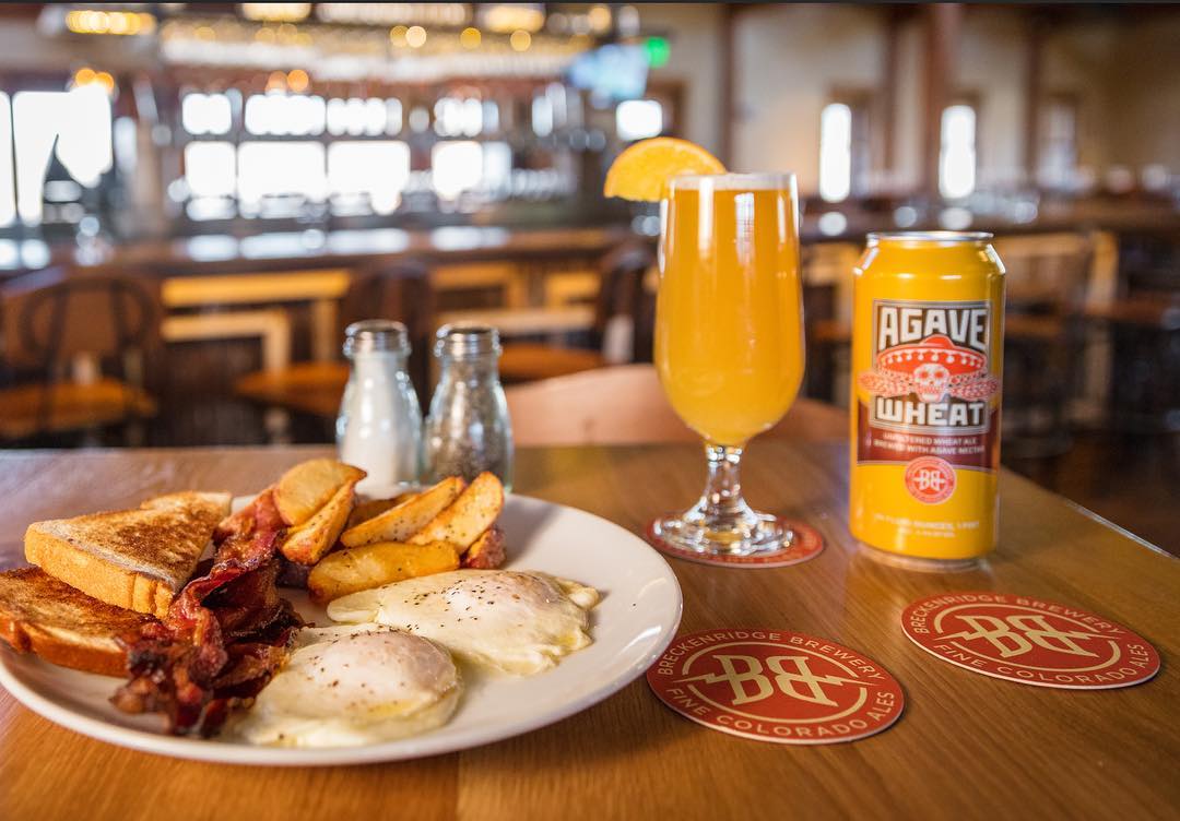 Plate of eggs, toast, bacon and potato wedges on a table alongside a glass of beer and a can Photo by Instagram user @breckbrewfarmhouse