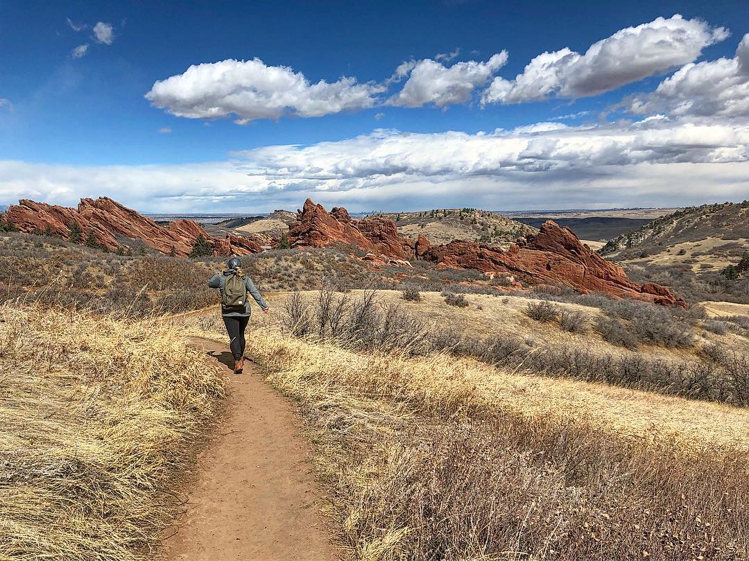 Woman walking on a dirt trail in outdoor Colorado with red rocks in the background Photo by Instagram user @melash