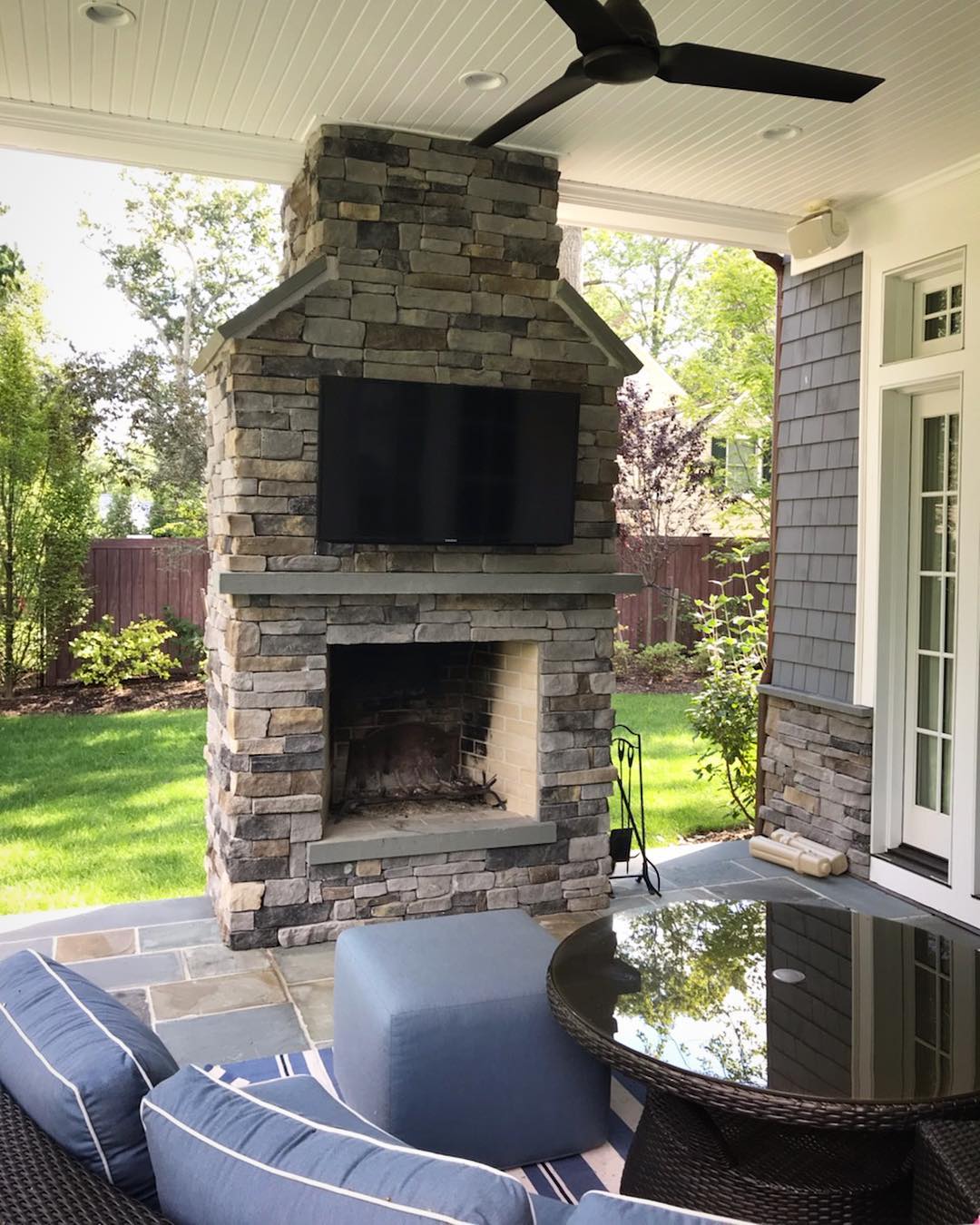 outdoor TV hanging from backyard fireplace with seating nearby photo by Instagram user @professional.audio.consultants
