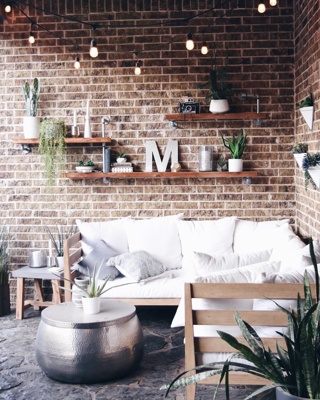 outdoor seating area with floating shelves set up on brick wall photo by Instagram user @pillowthoughthome