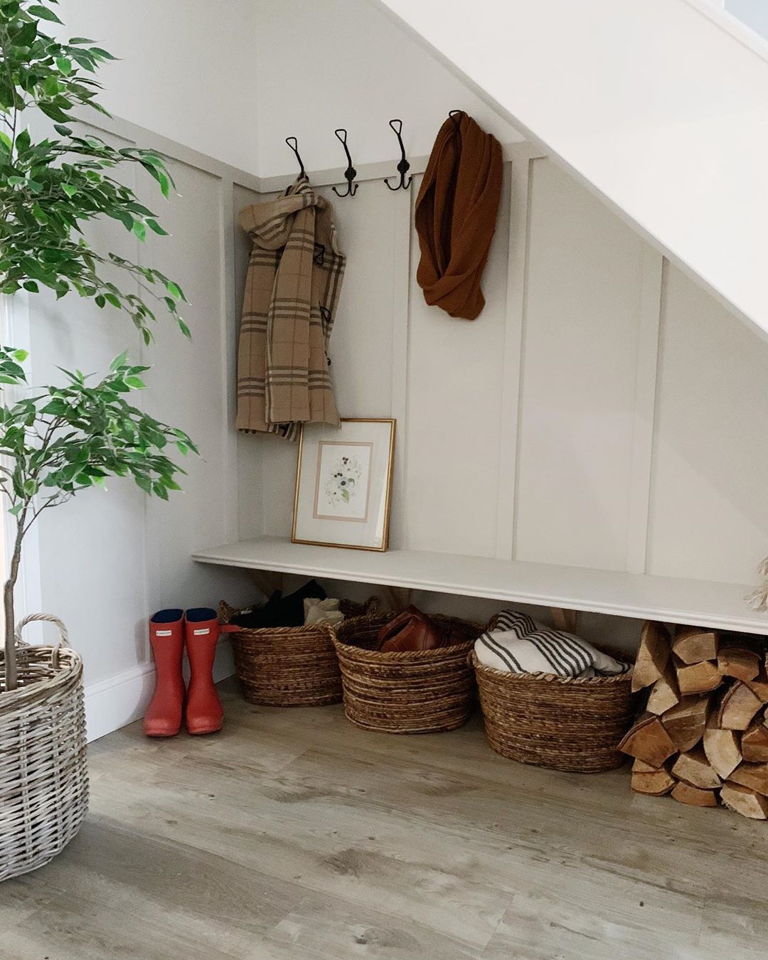 Small mud room with coat hangers and a bench with wicker baskets underneath.