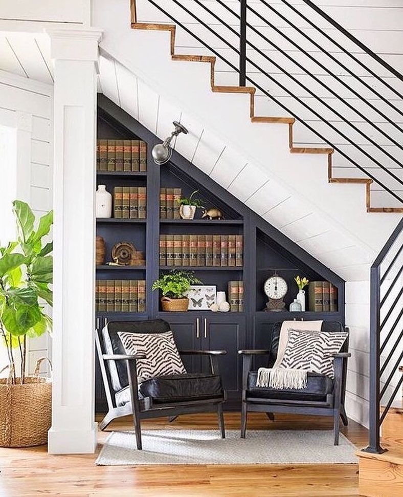 Small library made under home stairs with two chairs and a spotlight.