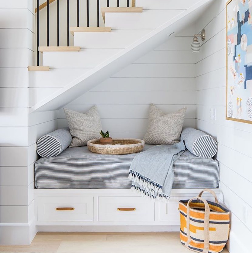 Small nook under the stairs with pillows and bench pad.