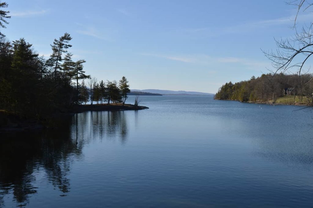 Shadowed view of dark blue lake with tree-covered shoreline in distance. Photo via Instagram user @mksestokas