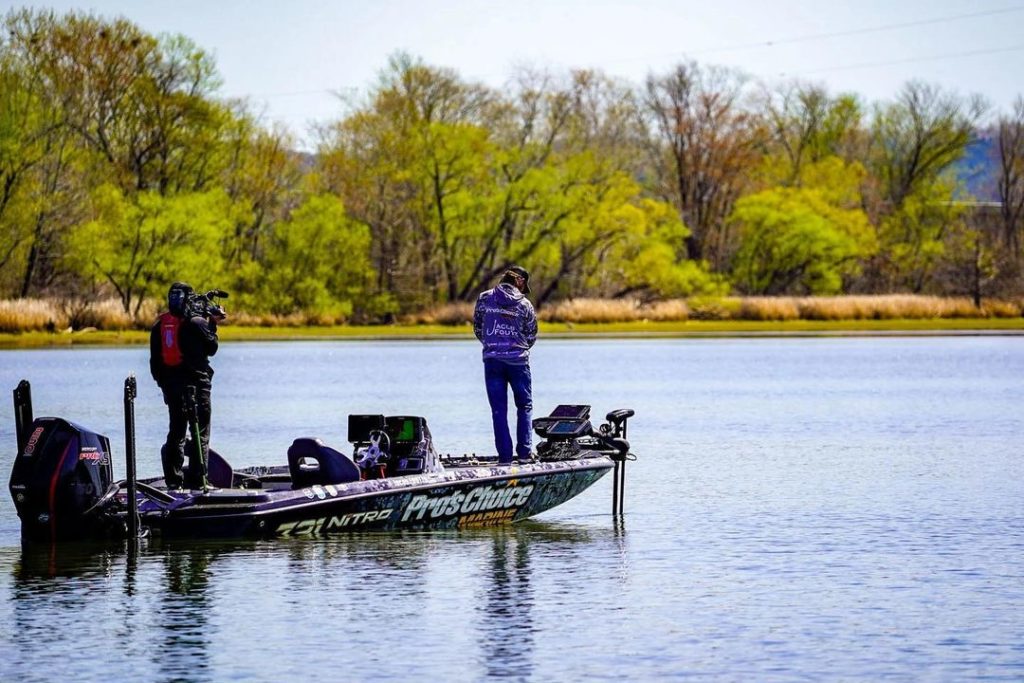 Two people in a boat preparing to fish on a sunny dat with trees on shoreline. Photo via Instagram user @jacobfoutzfishing