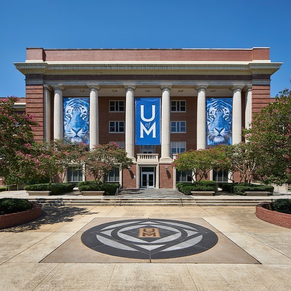 Photo of red brick building with white pillars and blue banners on the University of Memphis campus. Photo by Instagram user @uofmemphis