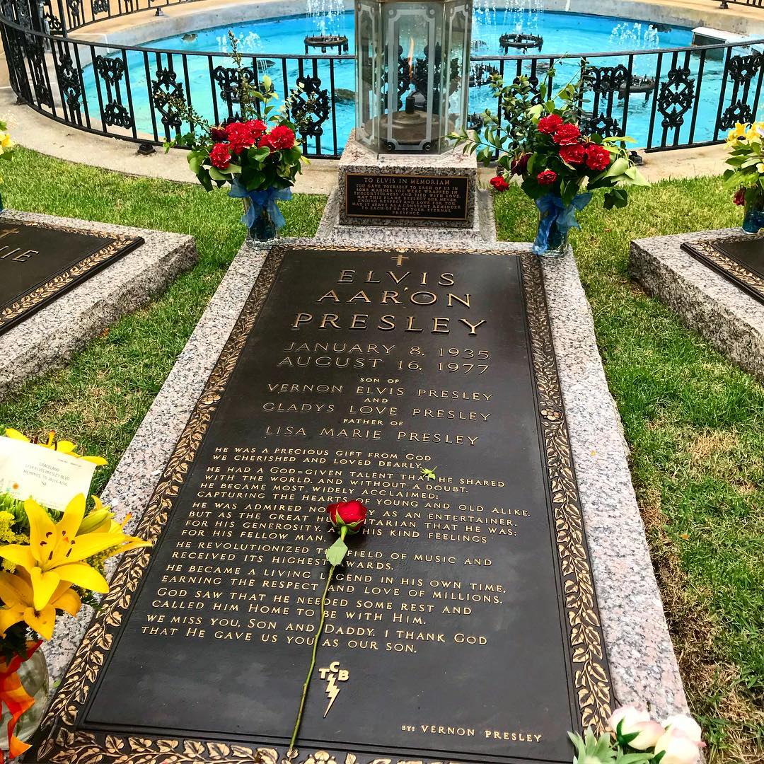 Elvis Presley's gravesite memorial with flowers at each corner and rose atop. Photo by Instagram user @ecrogers17