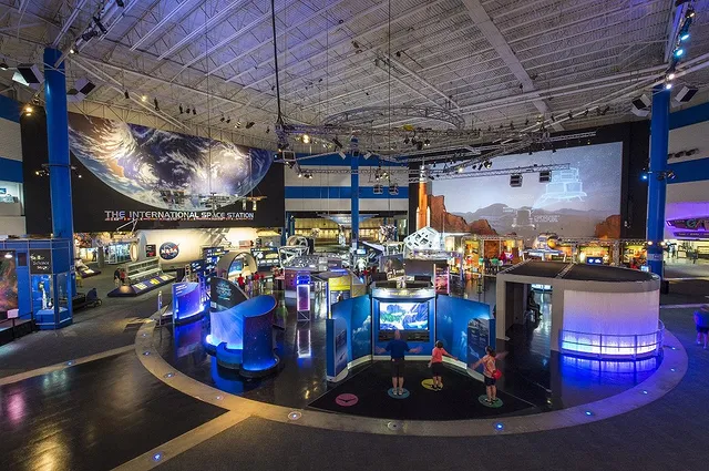 An interior shot of the Houston Space Center with a huge poster of earth, a screen showing the Mars rover, and many exhibits in the center of the room. Photo via Instagram user @spacecenterhou