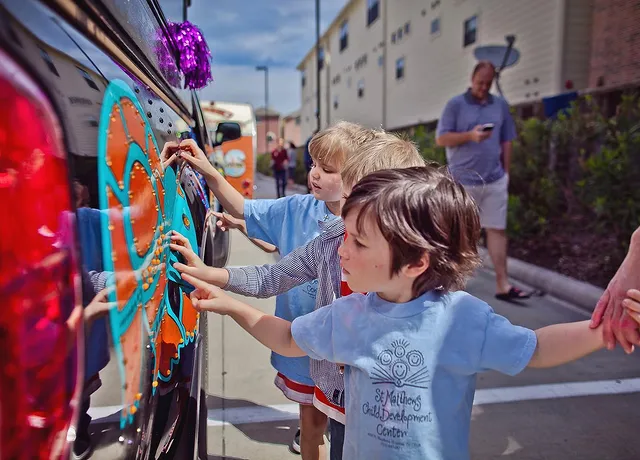 Young children touch the side of a car covered in paint and streamers at the art car parade on a sunny Houston day. Photo via Instagram user @theartcarparade