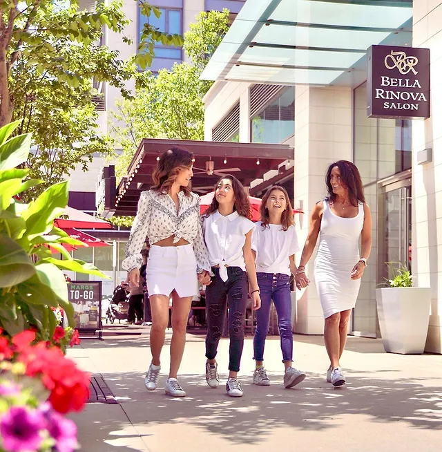 A group of girls and women in white outfits walk the sidewalks of Houston's River Oaks District on a sunny day in the summer with trees and flowers in the periphery. Photo via Instagram user @rodistrict