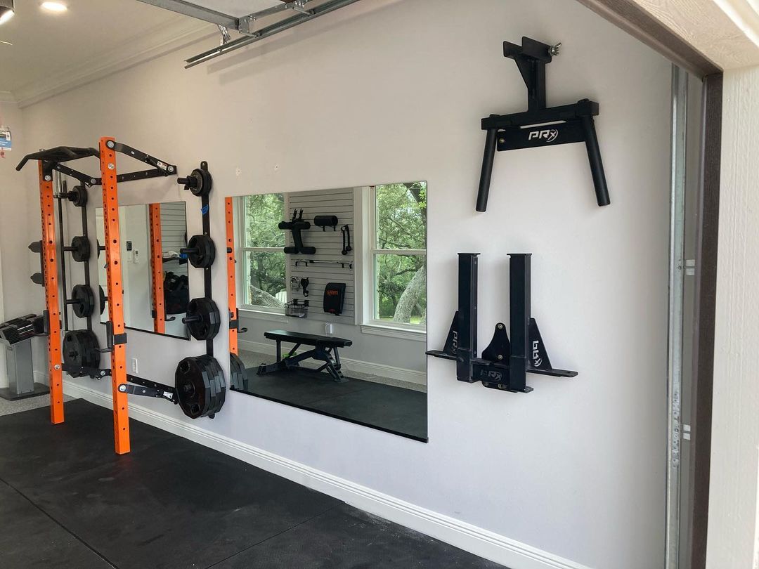 Home gym inside of garage with wall mounted mirrors. Photo by Instagram user @texasgaragegymbuilders.