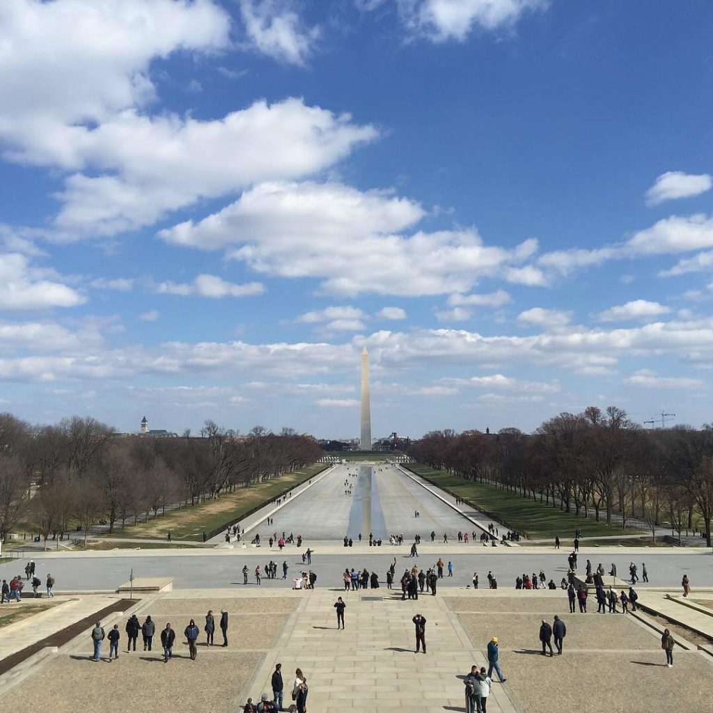Washington Monument with blue sky and tourists admiring Photo via @visitwashingtondc