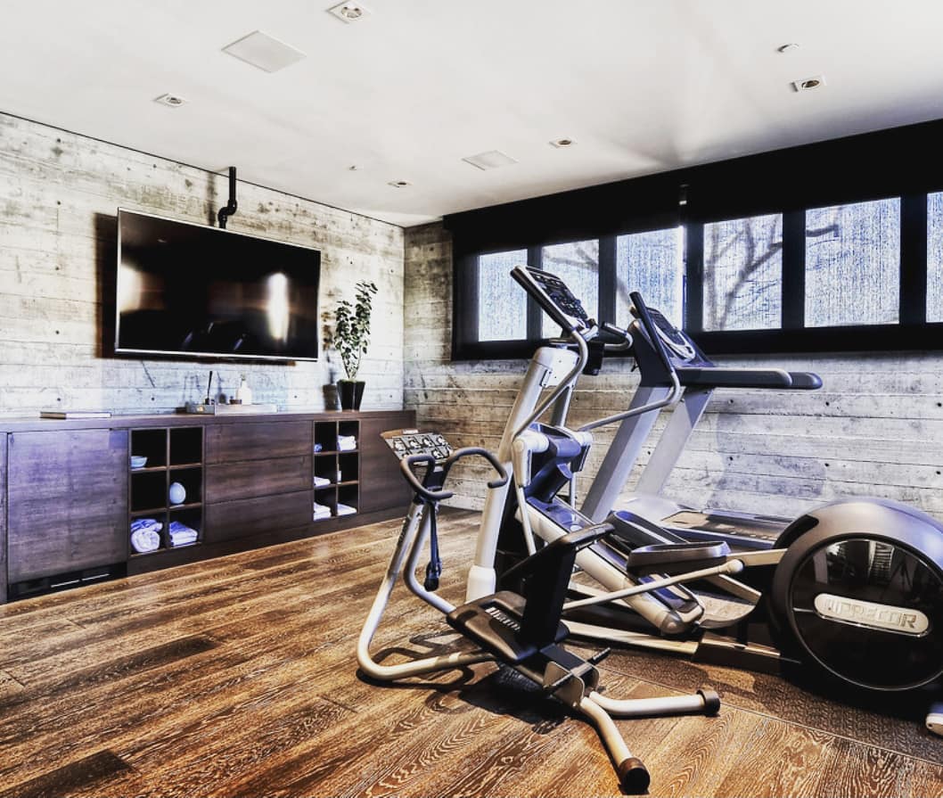 Home gym with flat screen TV and sound system in ceiling. Photo by Instagram user @coachdavecaplan.