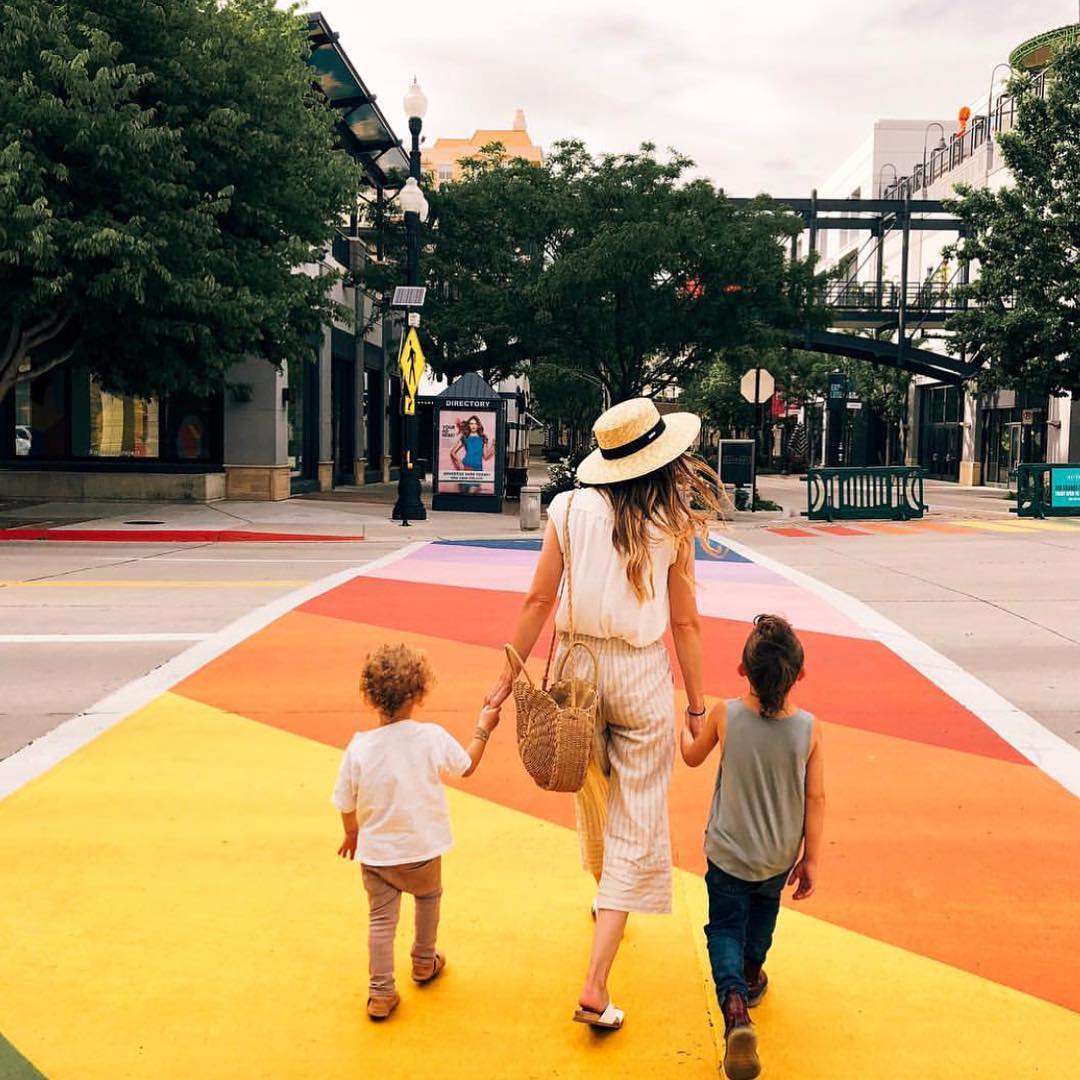 A woman and two young boys walk hand in hand across the street in a painted walkway. Photo by Instagram user @atthegateway