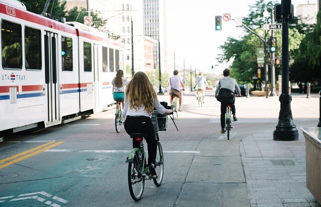 A woman, a man, and others bike through the street along side the rail train. Photo by Instagram user @slcbikeshare