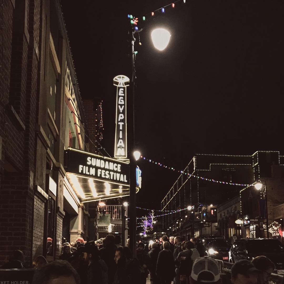 A crowd of people stand outside a theater as the signs for Sundance Film Festival light up above. Photo by Instagram user @sundanceorg