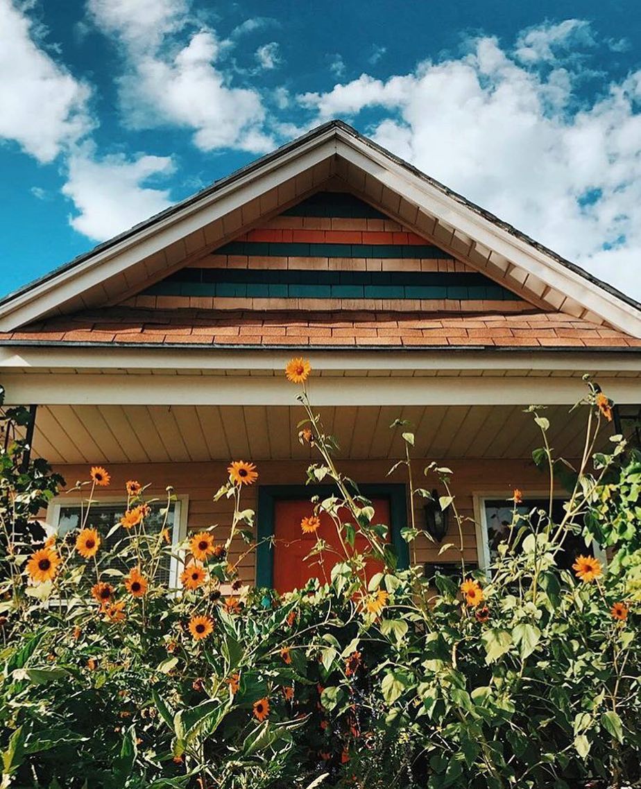 Old cottage style home with tall sunflowers growing in front of the porch. Photo by Instagram user @nikkiboliaux