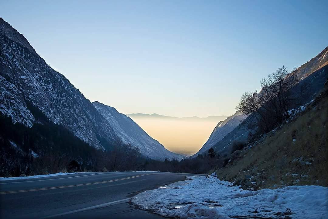 View of an empty road in between two mountains with the city off in the distance unerneath smog. Photo by Instagram user @oceanbabyinslc
